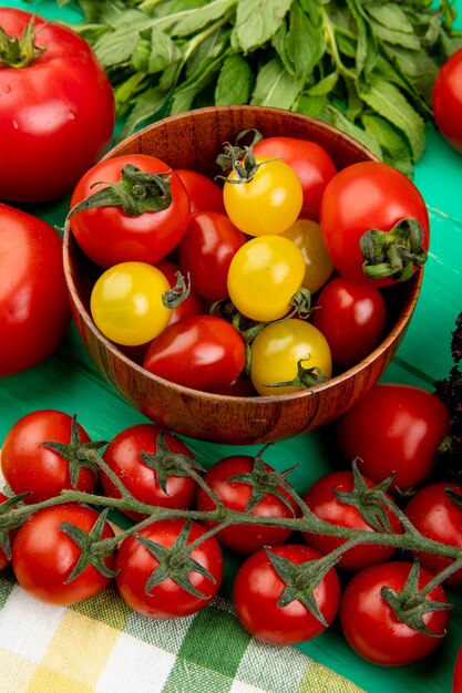 Vista laterale dei pomodori in ciotola con altri e foglie di menta verdi sulla tavola verde