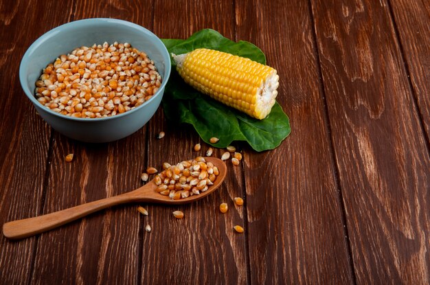 Vista laterale dei semi secchi del cereale in ciotola e cucchiaio di legno con mais e spinaci cucinati sulla tavola di legno con lo spazio della copia