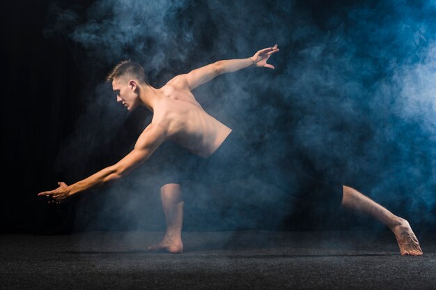 Vista laterale del ballerino che posa nel fumo