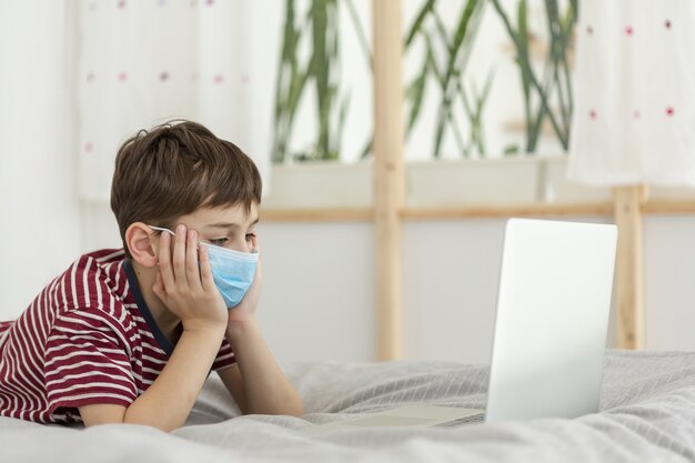 Vista laterale del bambino che indossa maschera medica e guardando portatile