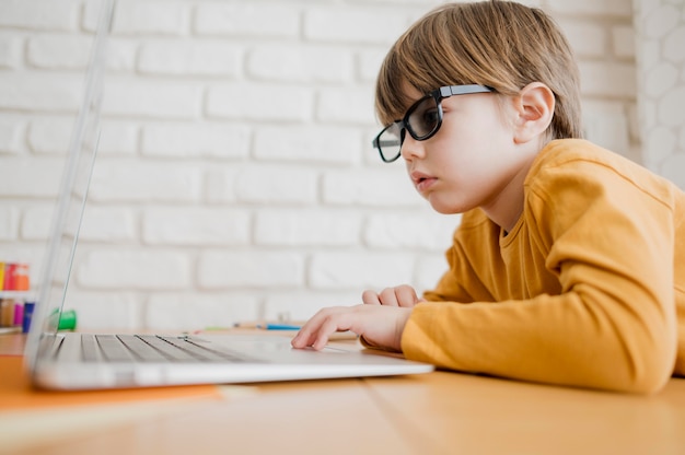 Vista laterale del bambino con i vetri che esamina computer portatile