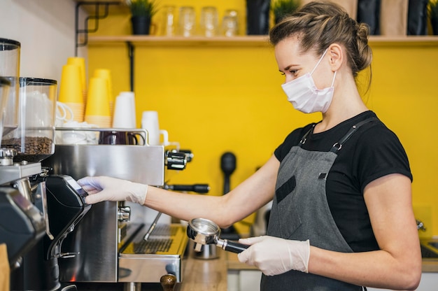 Vista laterale del barista femmina con guanti in lattice preparando il caffè per la macchina