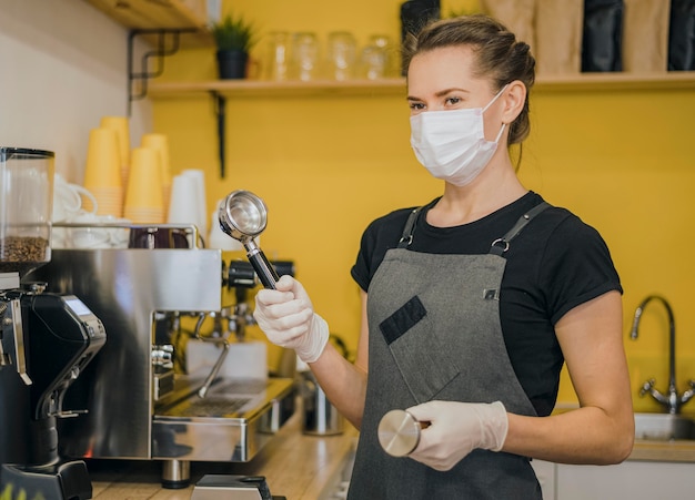 Vista laterale del barista femminile con la maschera medica che prepara caffè per la macchina