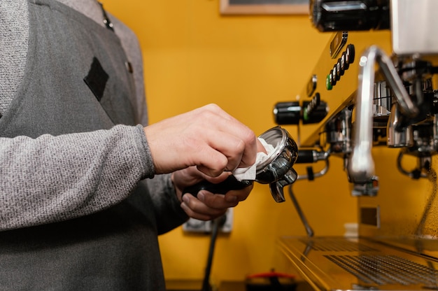 Vista laterale del barista maschio con macchina da caffè professionale per la pulizia del grembiule