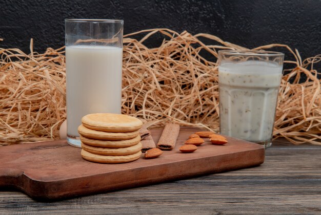 vista laterale del bicchiere di latte e biscotti mandorle sul tagliere sulla superficie in legno e parete nera