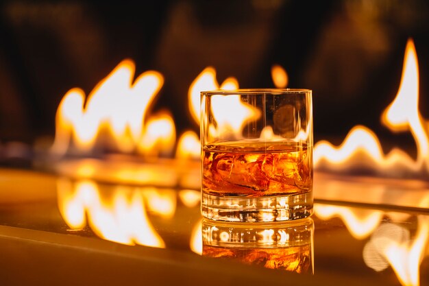 Vista laterale del bicchiere di whisky con ghiaccio su uno sfondo di una fiamma che brucia