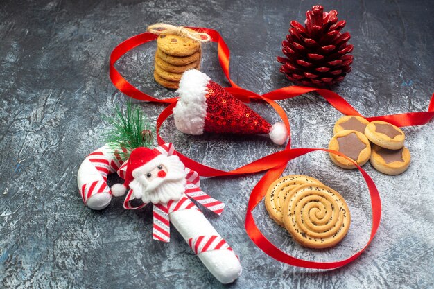 Vista laterale del cappello di babbo natale e biscotti regalo con conifere rosso cioccolato cornel su superficie scura