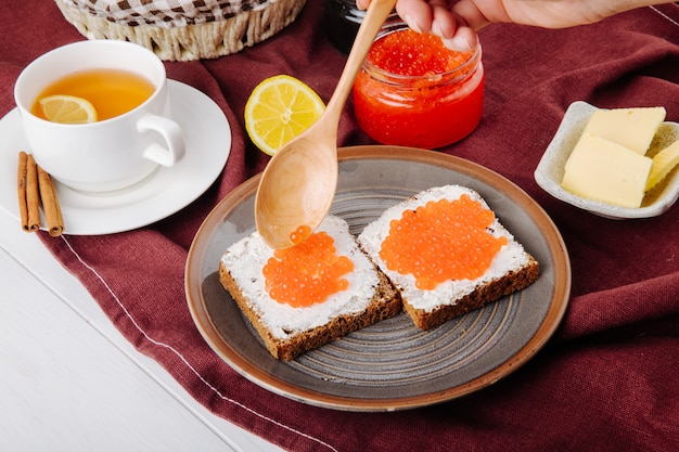 Vista laterale del caviale rosso toast pane di segale con ricotta tazza di burro di caviale rosso di tè e fetta di limone sul tavolo