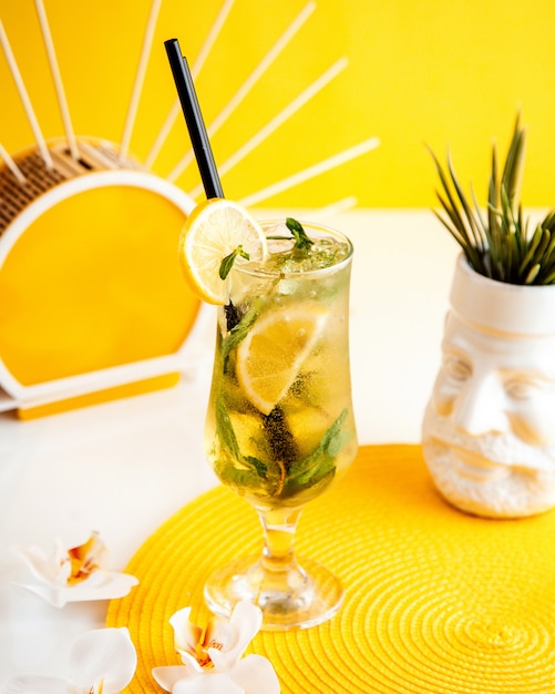 Vista laterale del cocktail mojito con ghiaccio e limone in un bicchiere su giallo