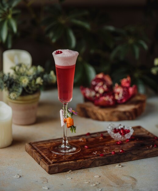 Vista laterale del cocktail rosso dell'alcool con i fagioli del melograno su un bordo di legno sulla tavola