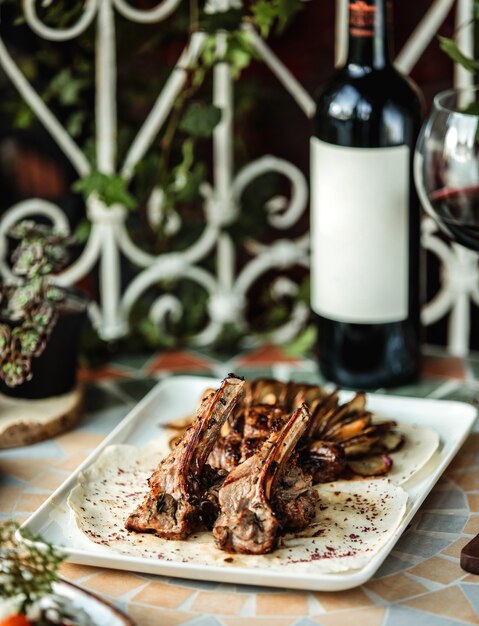 Vista laterale del costolette di agnello kebab con patate al forno sul tavolo con una bottiglia di vino rosso