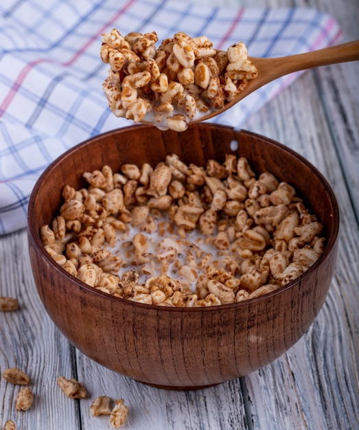 Vista laterale del cucchiaio e della ciotola di legno con riso dolce soffiato su rustico