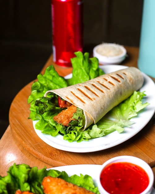 Vista laterale del doner di pollo avvolta in lavash su lattuga sulla tavola di legno