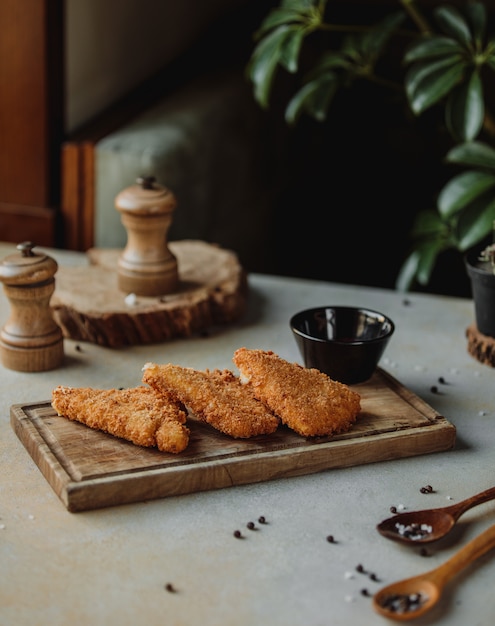 Vista laterale del filetto di pollo fritto nella briciola di pane con salsa su un bordo di legno