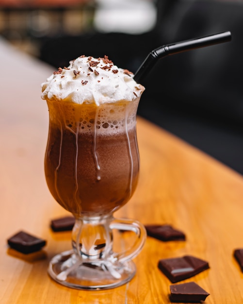 Vista laterale del frappé del cioccolato con panna montata in un vetro su una tavola di legno