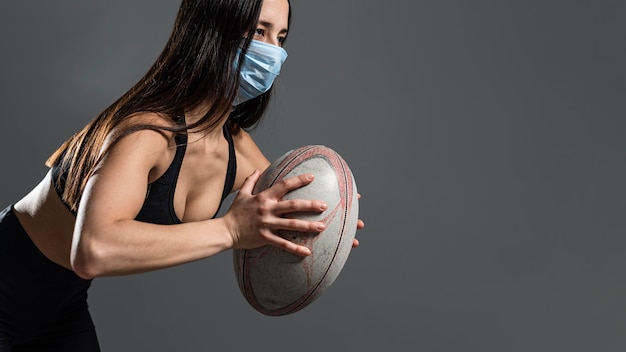 Vista laterale del giocatore di rugby femminile atletico che tiene palla mentre indossa la maschera medica