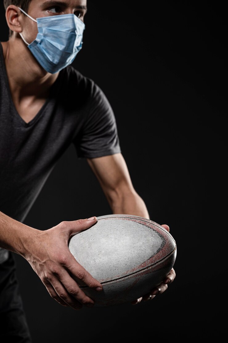 Foto gratuito vista laterale del giocatore di rugby maschile con palla medica maschera tenendo