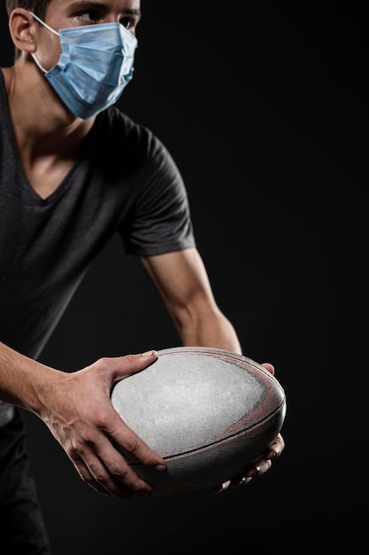 Vista laterale del giocatore di rugby maschile con palla medica maschera tenendo