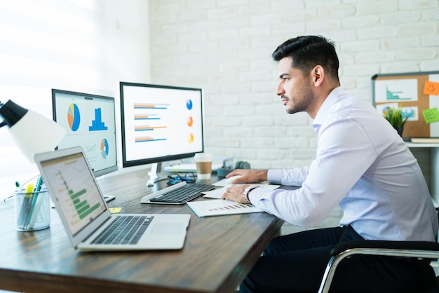 Vista laterale del giovane uomo d'affari attraente che studia i grafici sul computer mentre lavora a casa