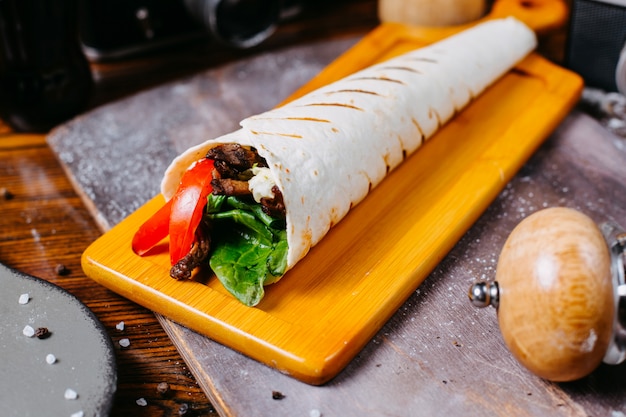 Vista laterale del kebab del doner spostata nel lavash sul bordo di legno