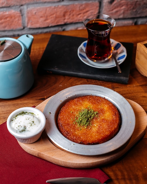 Vista laterale del kunefe turco tradizionale del dessert con polvere di pistacchio e formaggio su una tavola di legno