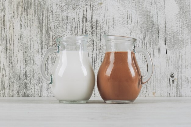 Vista laterale del latte di cacao e del bicchiere di latte su un fondo di legno bianco