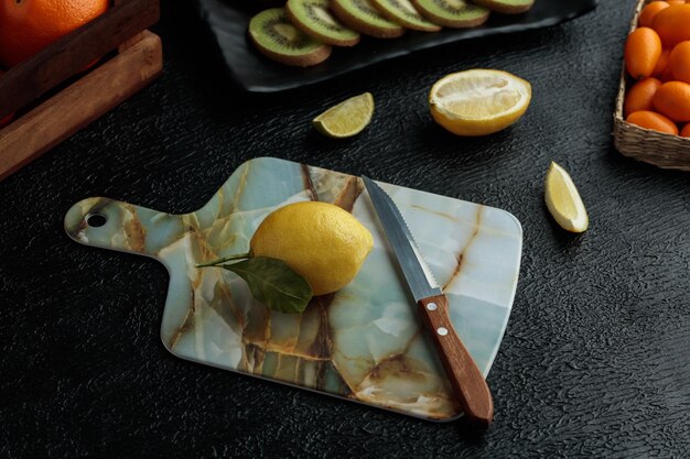 Vista laterale del limone con il coltello sul tagliere con fette di kiwi fetta di lime tagliata limone e kumquat interi su sfondo nero