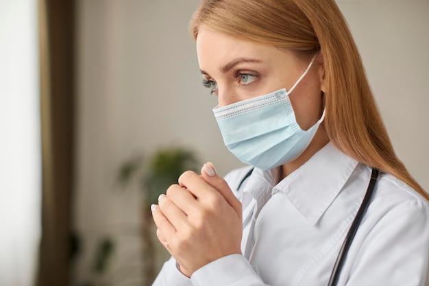 Vista laterale del medico femminile del centro di recupero covid con la preghiera della mascherina medica