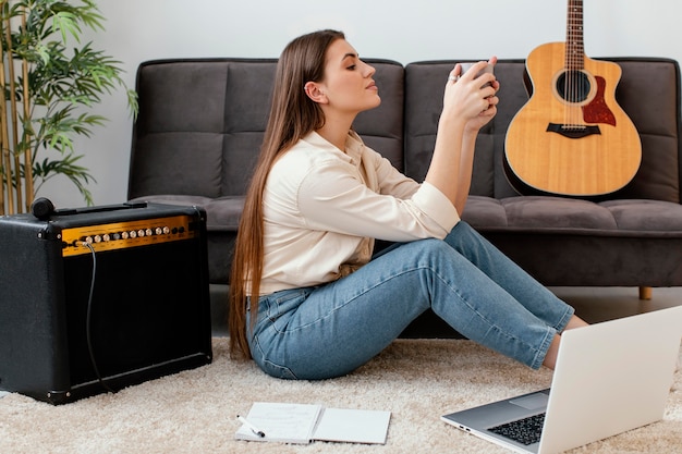 Vista laterale del musicista femminile che tiene la tazza accanto alla chitarra acustica