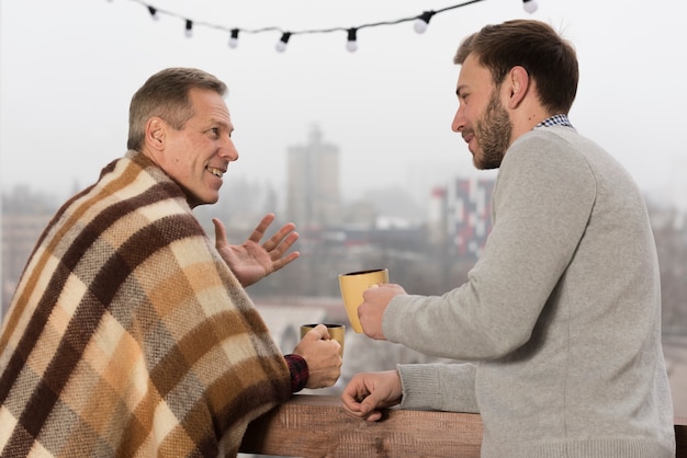 Vista laterale del padre con coperta e figlio tenendo tazze in mano