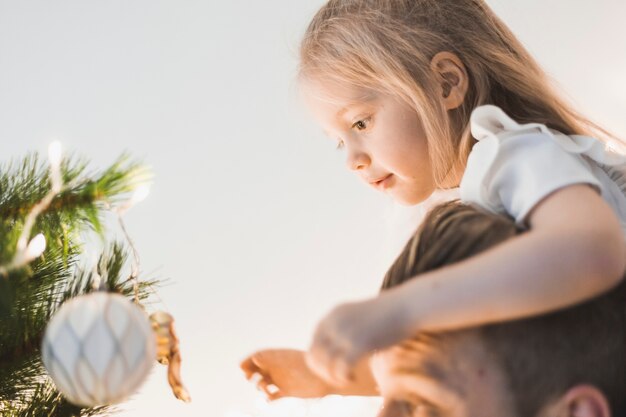 Vista laterale del padre e della ragazza che esaminano l&#39;albero di Natale illuminato