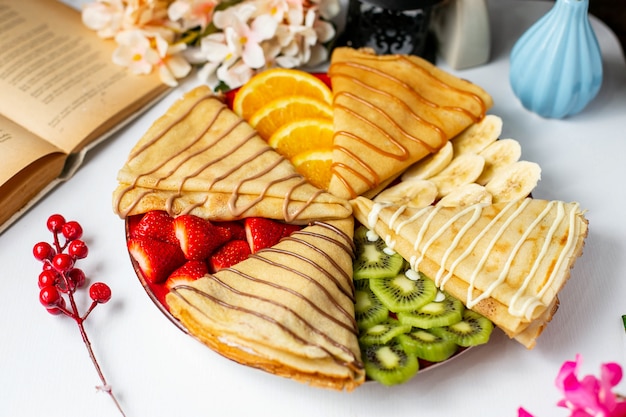 Vista laterale del pancake con frutta e salsa di cioccolato al latte sul tavolo