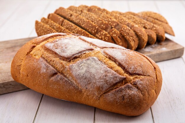 Vista laterale del pane come pannocchia con semi marrone a fette sul tagliere e pane croccante su sfondo di legno