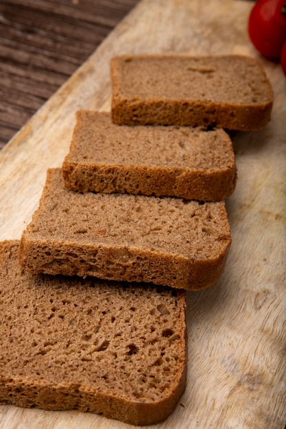 Vista laterale del pane di segale affettato su superficie e su fondo di legno