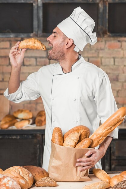 Vista laterale del panettiere maschio che mangia la pagnotta fresca della tenuta del croissant