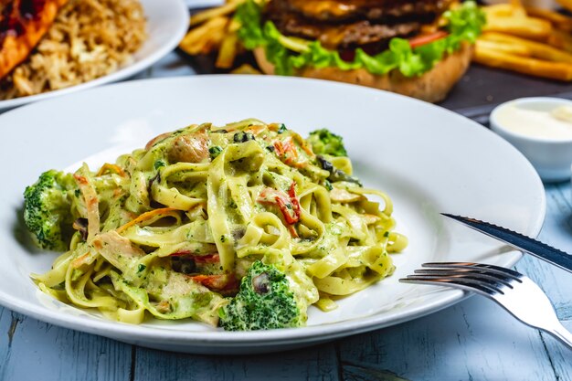 Vista laterale del pepe delle spezie della salsa cremosa del pollo dei broccoli della pasta di Fettuccine