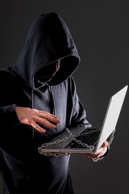 Vista laterale del pirata informatico maschio con il computer portatile protetto dalla catena del metallo