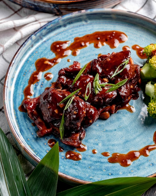 Vista laterale del pollo arrosto con salsa agrodolce e broccoli su un piatto sulla tovaglia plaid