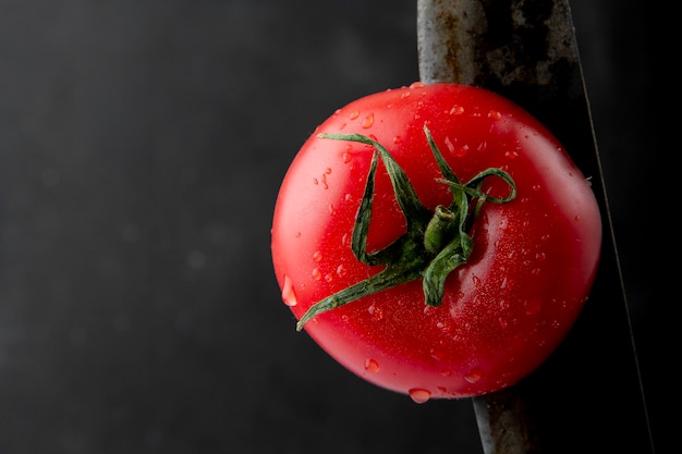 Vista laterale del pomodoro bagnato maturo con un coltello a fondo nero