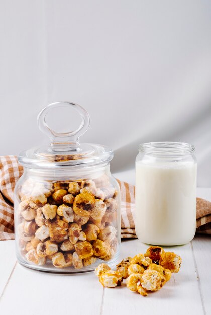 Vista laterale del popcorn al caramello dolce in un barattolo di vetro su fondo di legno bianco