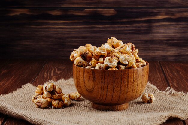 Vista laterale del popcorn al caramello dolce in una ciotola di legno su fondo rustico