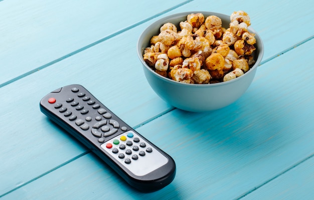 Vista laterale del popcorn al caramello dolce in una ciotola e tv a distanza su sfondo blu