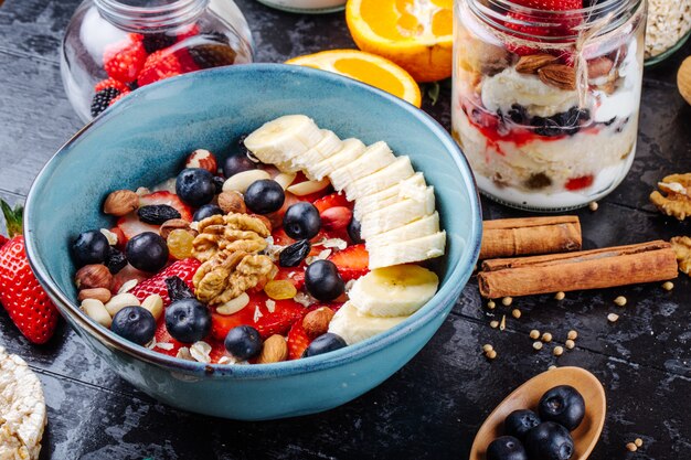 Vista laterale del porridge di farina d'avena con fragole mirtilli banane frutta secca e noci in una ciotola di ceramica sul tavolo