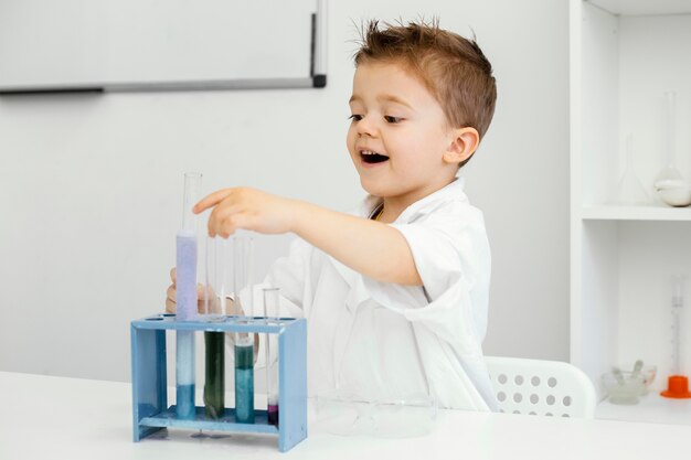 Vista laterale del ragazzo scienziato in laboratorio facendo esperimenti con provette