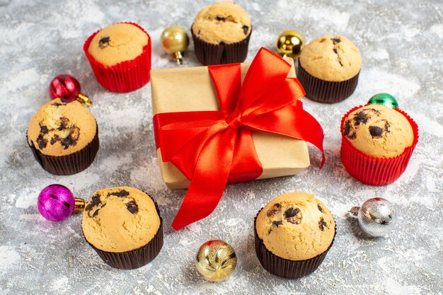 Vista laterale del regalo con nastro rosso tra deliziosi piccoli cupcakes appena sfornati e accessori decorativi sul tavolo del ghiaccio
