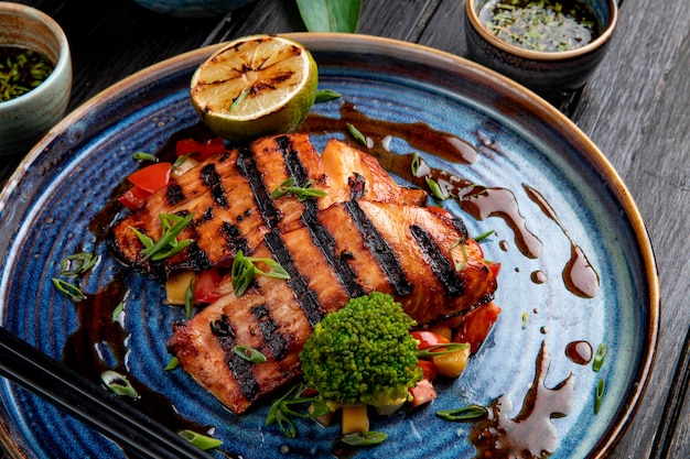 Vista laterale del salmone arrostito con le verdure limone e salsa di soia su un piatto sulla tavola di legno