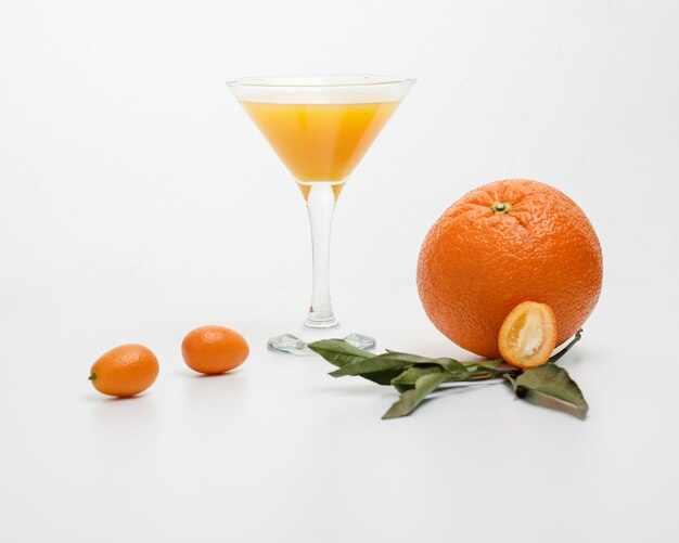 Vista laterale del succo d'arancia in vetro con arancia e kumquat con foglie su sfondo bianco