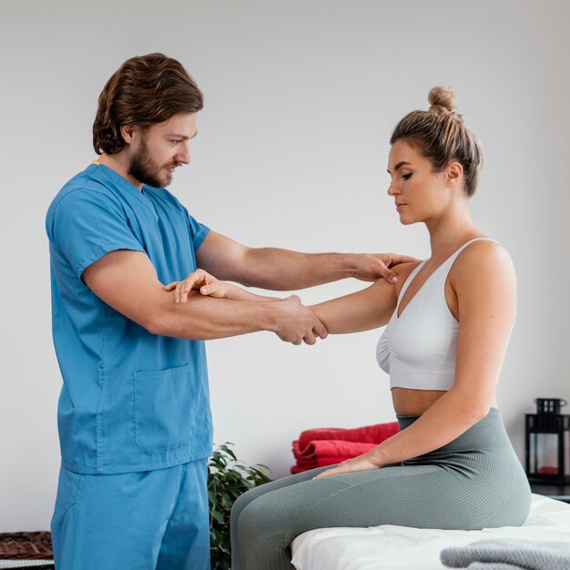 Vista laterale del terapista osteopatico maschio che controlla la spalla del paziente femminile