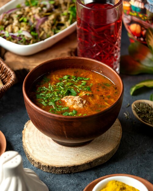 Vista laterale del tradizionale borscht rosso russo o ucraino con manzo e verdure-barbabietola patate carota cipolla cavolo erbe fresche e spezie in ciotola di argilla su bla