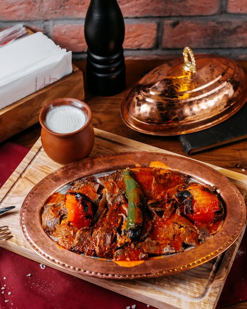 Vista laterale del tradizionale doner turco iskender con yogurt in un vaso di terracotta su una tavola di legno